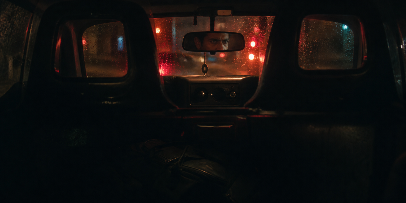 An anxious cab driver reflected in the rear-view mirror on a rainy London night